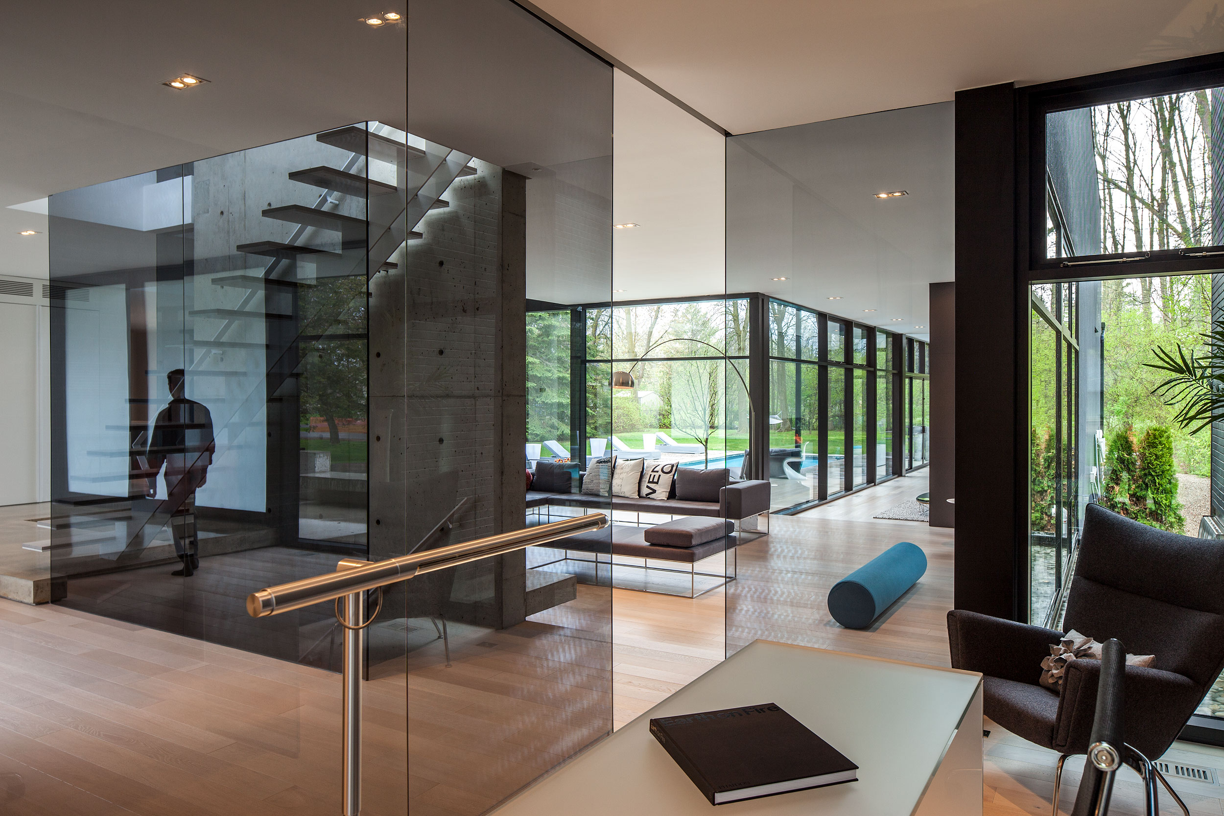 Glass walls, blond hardwood floors, reflection of a floating staircase, view in to the backyard, swimming pool, trees, lawn of a ultra modern house architectural photography by Peter A. Sellar 