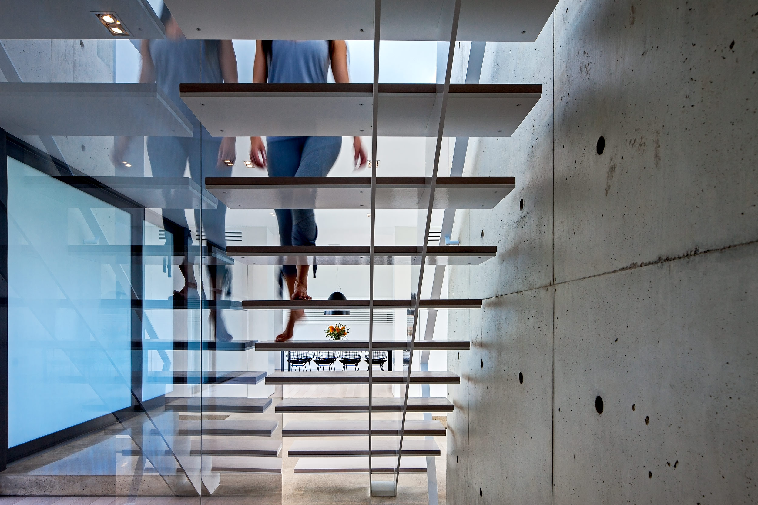 A woman walking up a floating staircase in an ultra modern home architectural photography by Peter A. Sellar
